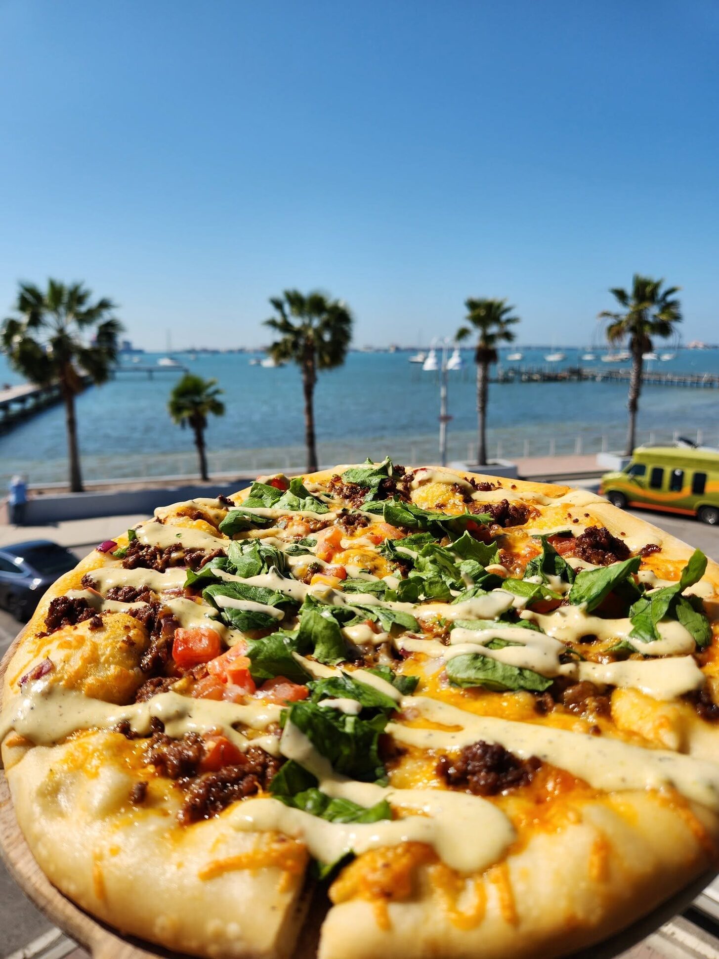 A pizza on the O'Maddy's rail, with palms, sailboats and Boca Ciega Bay behind