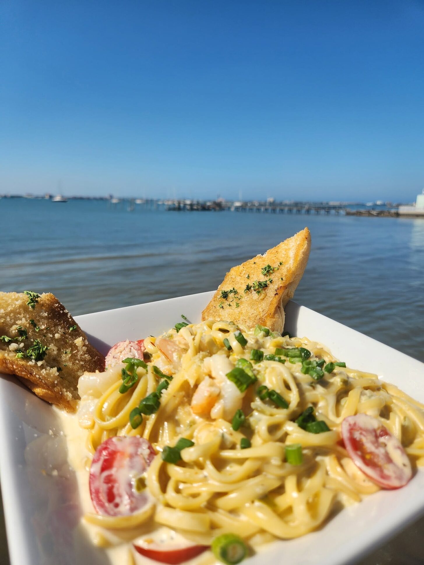 A pasta plate on the O'Maddy's rail, with the bay and the Gulfport pier behind