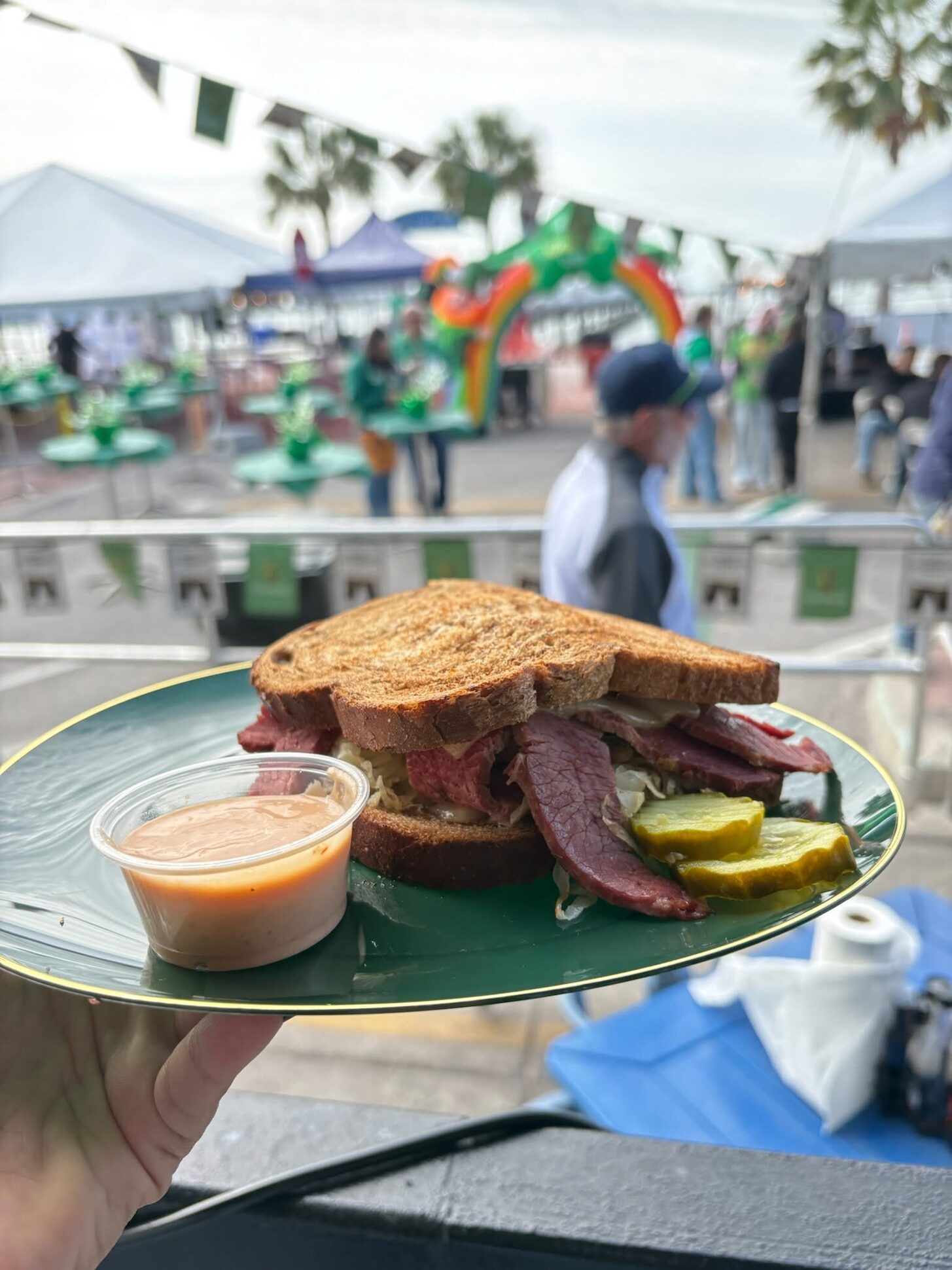 A Reuben on rye with a pickle, held up outdoors
